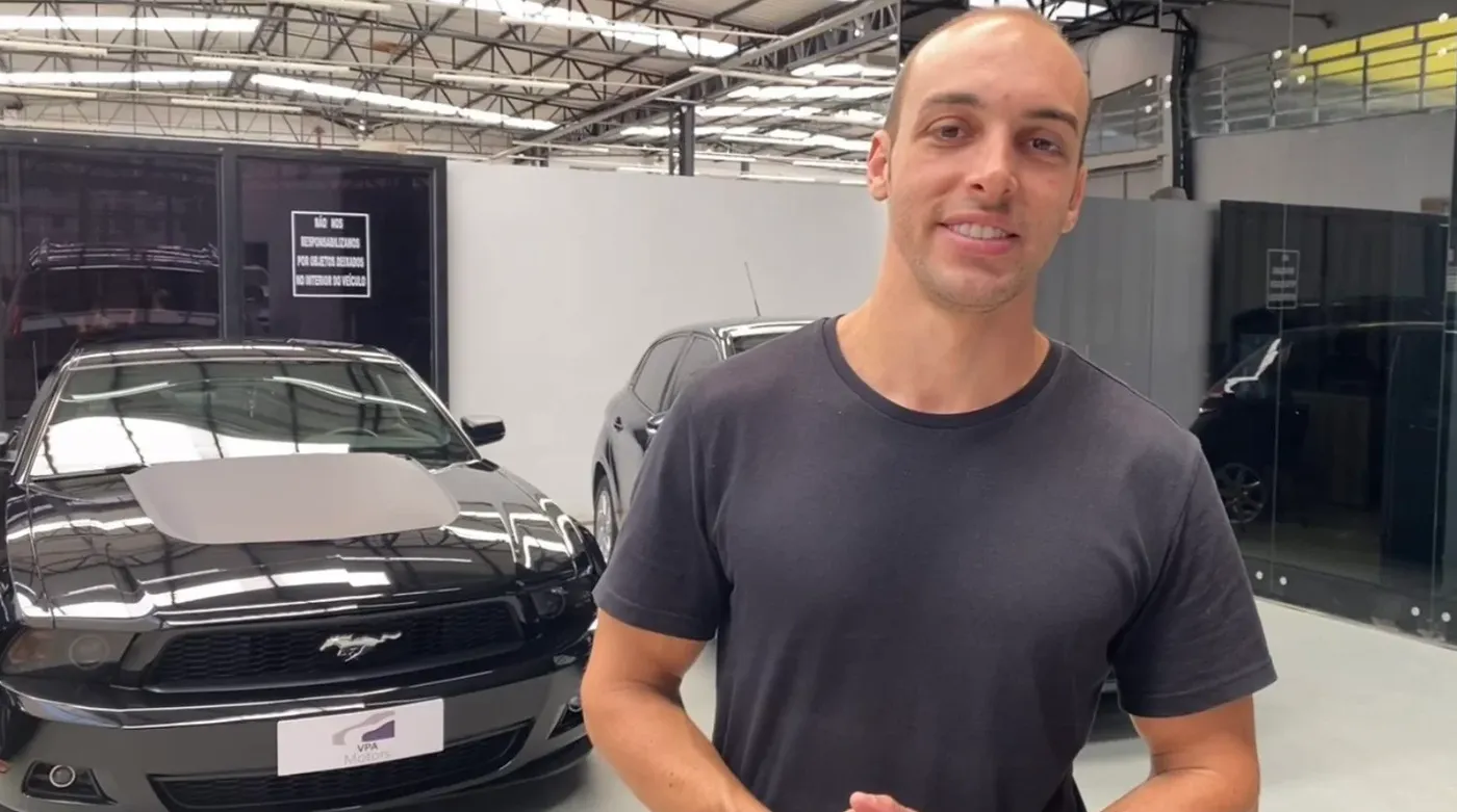 Quadro do vídeo de apresentação da VPA, gravado na oficina, com um Mustang preto ao fundo